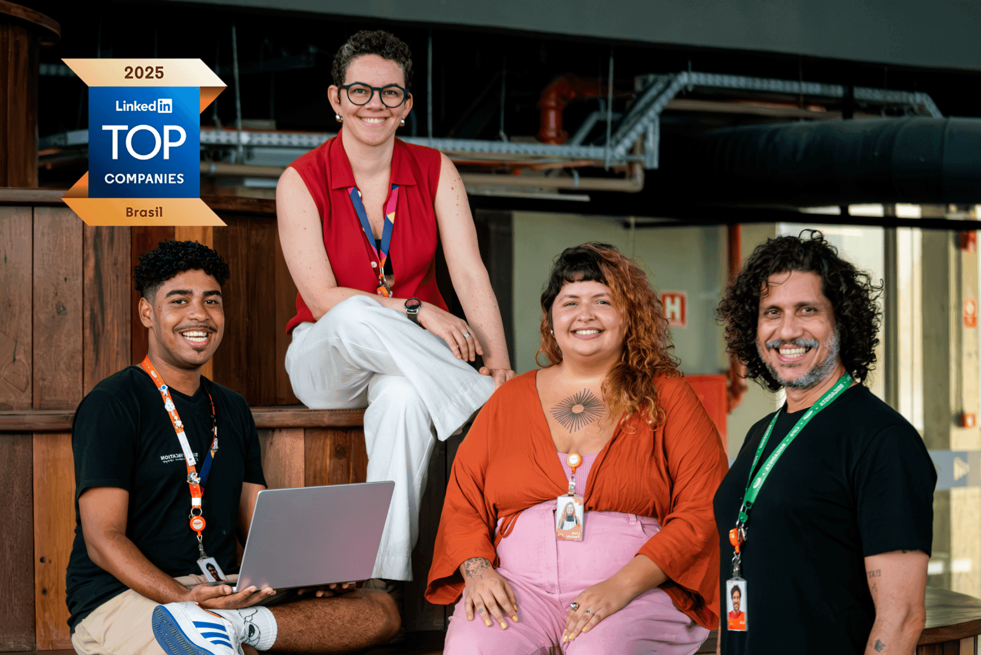 cesar-linkedin-top-company-melhores-empresas (3) Quatro funcionários sorrindo sentados em uma escada de madeira, com um logotipo do LinkedIn "Top Companies Brasil 2025" ao fundo.