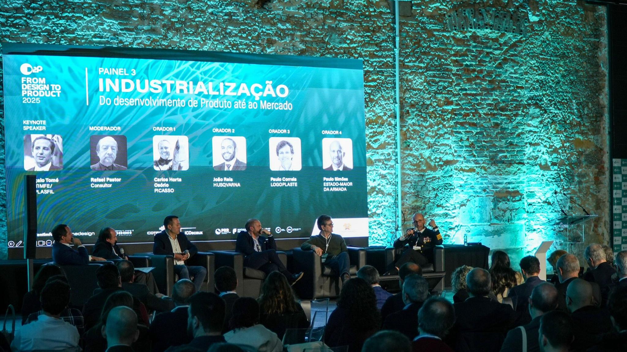 d2p-evento-design-indutria-produtos-cesar (2) Painel de discussão "Industrialização: Do desenvolvimento de produto ao mercado", com vários palestrantes e moderador, em frente a uma parede de tijolos iluminada.