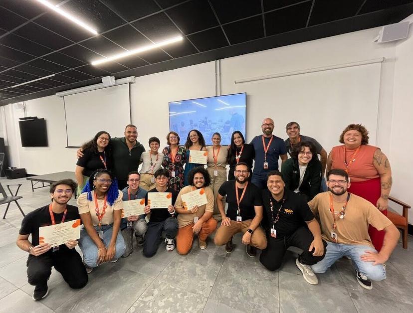 Petrobras e CESAR – Equipe celebra projeto de inovação corporativa Grupo de 18 profissionais sorridentes segura certificados em sala de treinamento, celebrando a conclusão de projeto de inovação
