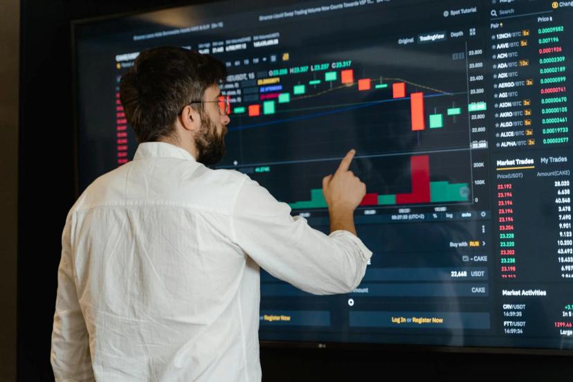 Open Finance IA e UX como pilares para inovar o setor financeiro Analista aponta para tela grande exibindo gráficos de velas e dados de mercado financeiro em tempo real em ambiente escuro.