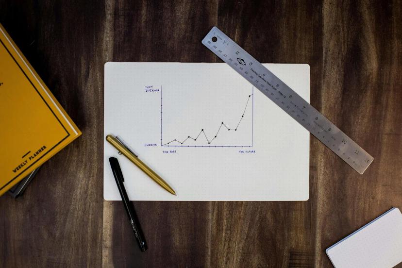 Inovação em P&D com Quick Win para acelerar resultados na indústria Gráfico desenhado à mão em papel branco mostrando linha de crescimento ascendente, cercado por régua, canetas e agenda.