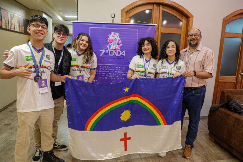 Grupo de estudantes e professor segura a bandeira de Pernambuco durante a 7ª Olimpíada Nacional de Aplicativos.