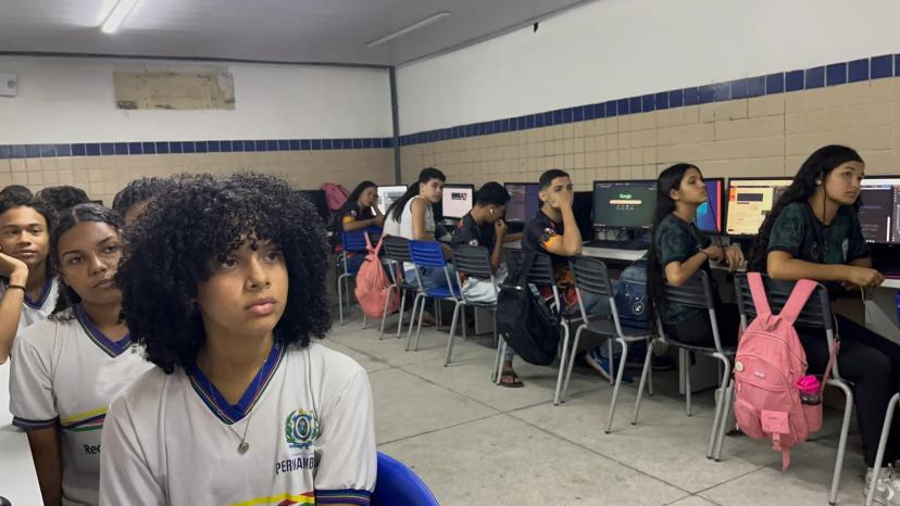 Empregabilidade jovem e o impacto social da inclusão digital em Pernambuco Grupo de jovens em laboratório de informática escolar, sentados em frente a computadores de mesa, usando uniformes de Pernambuco.