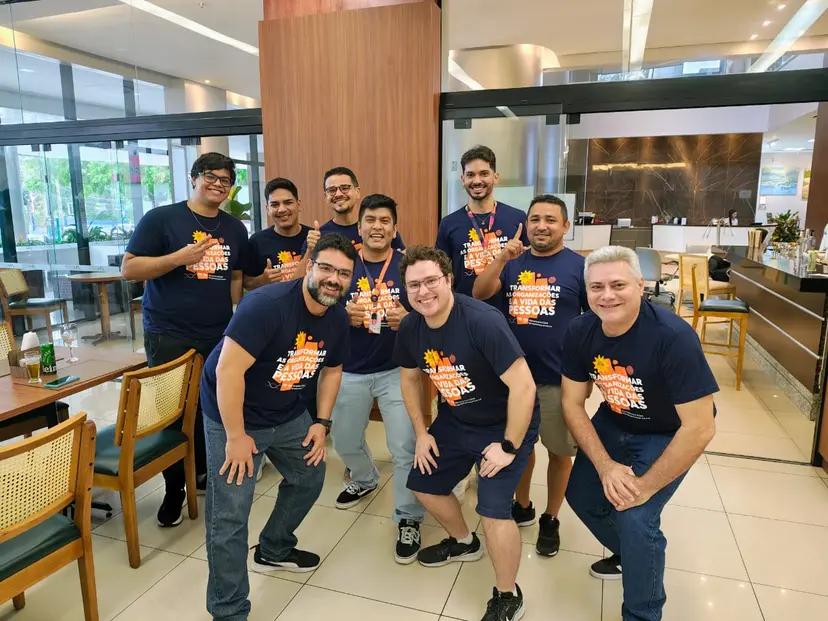 LG e CESAR criam solução de auditoria inteligente de escala global Nove homens sorridentes com t-shirts azuis iguais posam num restaurante. A frase na camisa foca na transformação de pessoas.