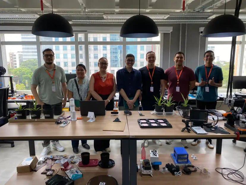 CBA transforma dados em sustentabilidade atraves do monitoramento do solo Sete profissionais posam atrás de bancadas com mudas de plantas e componentes eletrônicos num laboratório moderno