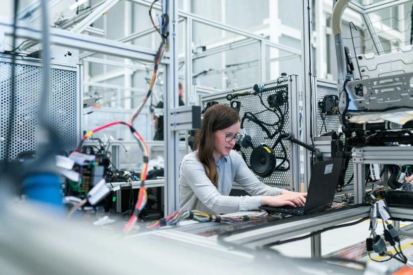 Asset inspection with AI and computer vision revolutionizing industry Woman wearing glasses using a laptop inside an industrial laboratory surrounded by complex wiring and metal structures.