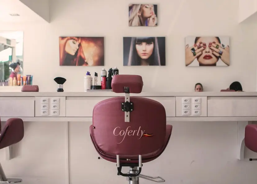 Cadeira de salão bordô com logo Coferly em destaque. Ao fundo, bancada branca com produtos e quadros de modelos na parede