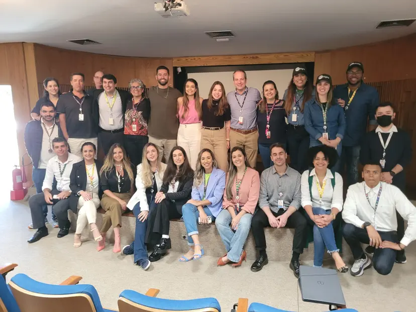 Grupo de cerca de 25 profissionais sorridentes posam juntos em um auditório durante o Bootcamp SBT de inovação