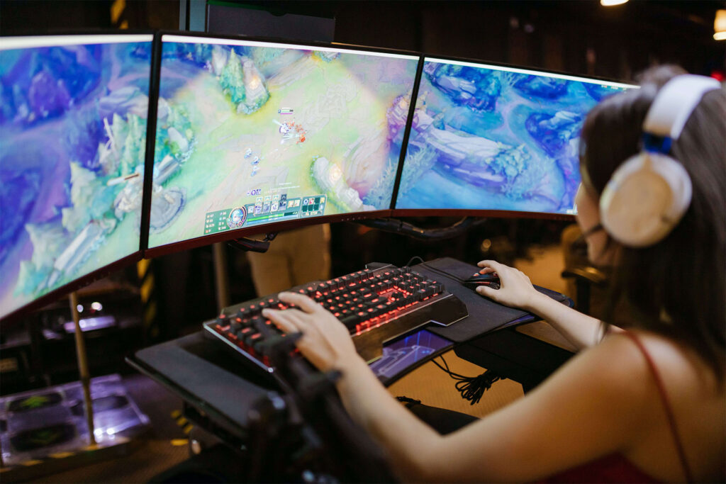 Woman playing League of Legends on a computer with three monitors.
