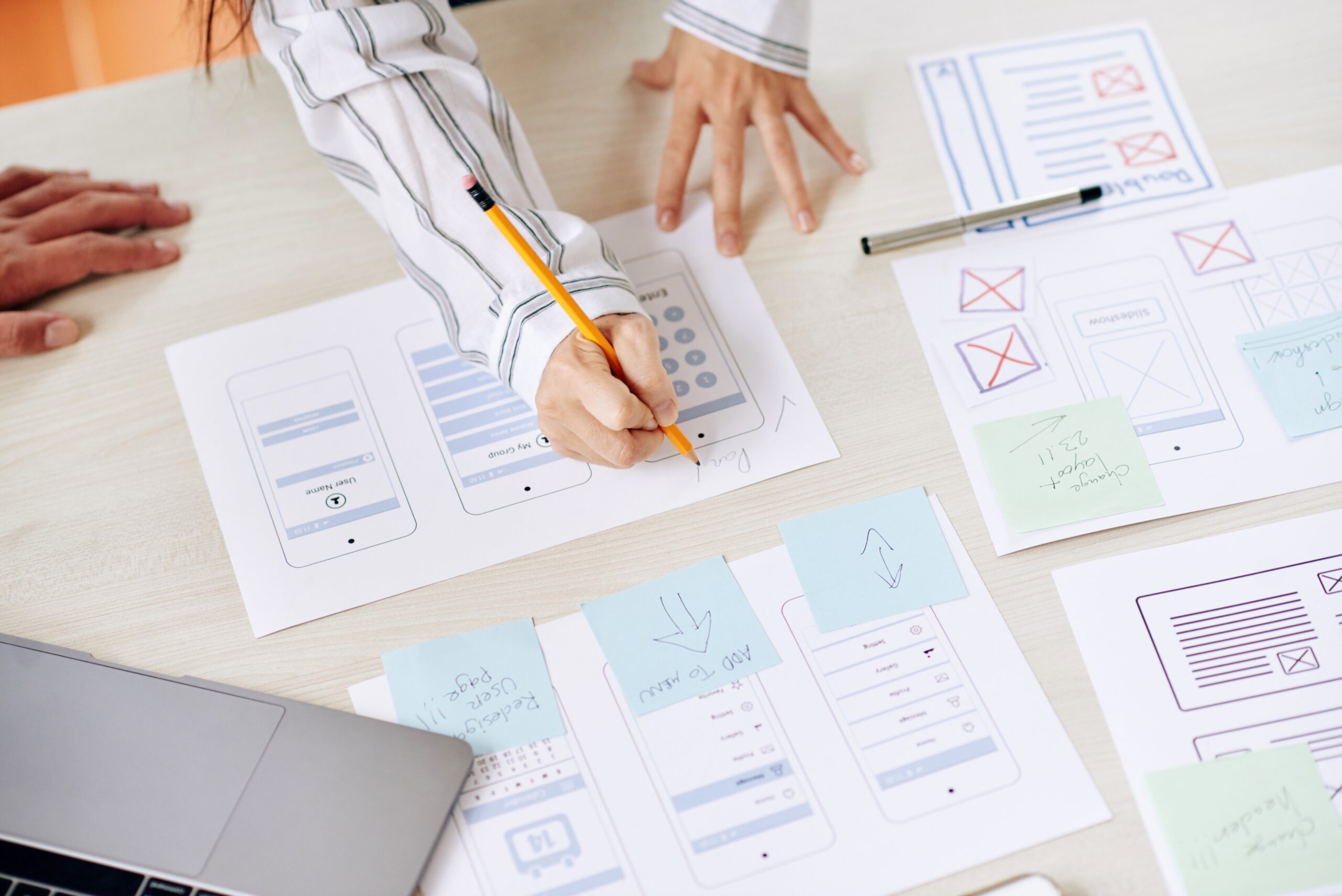 Duas designers revisam esboços de protótipos de aplicativos para celular, anotando melhorias em papeis com caneta e post-its.