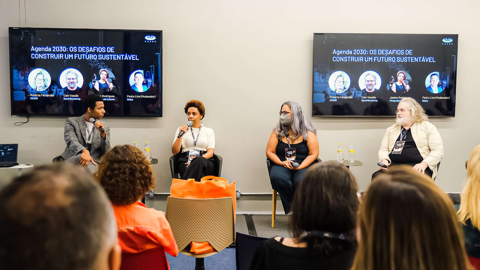 Um evento com quatro pessoas palestrando, com uma plateia