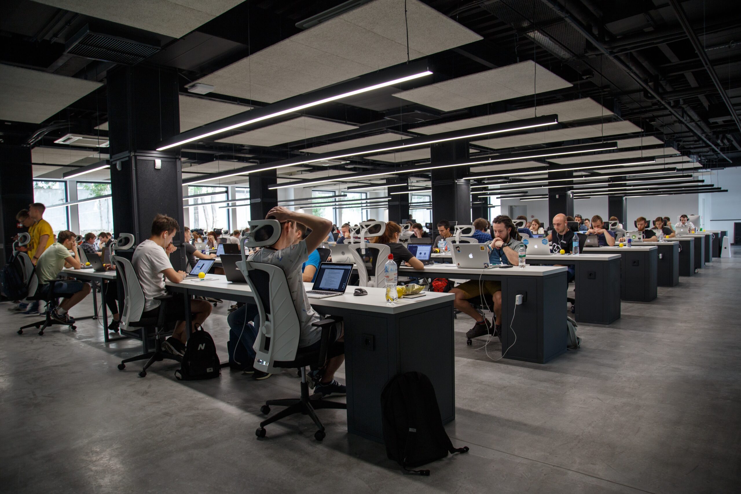 Uma grande sala de escritório moderna e aberta, com muitos funcionários sentados em suas mesas, trabalhando em computadores.