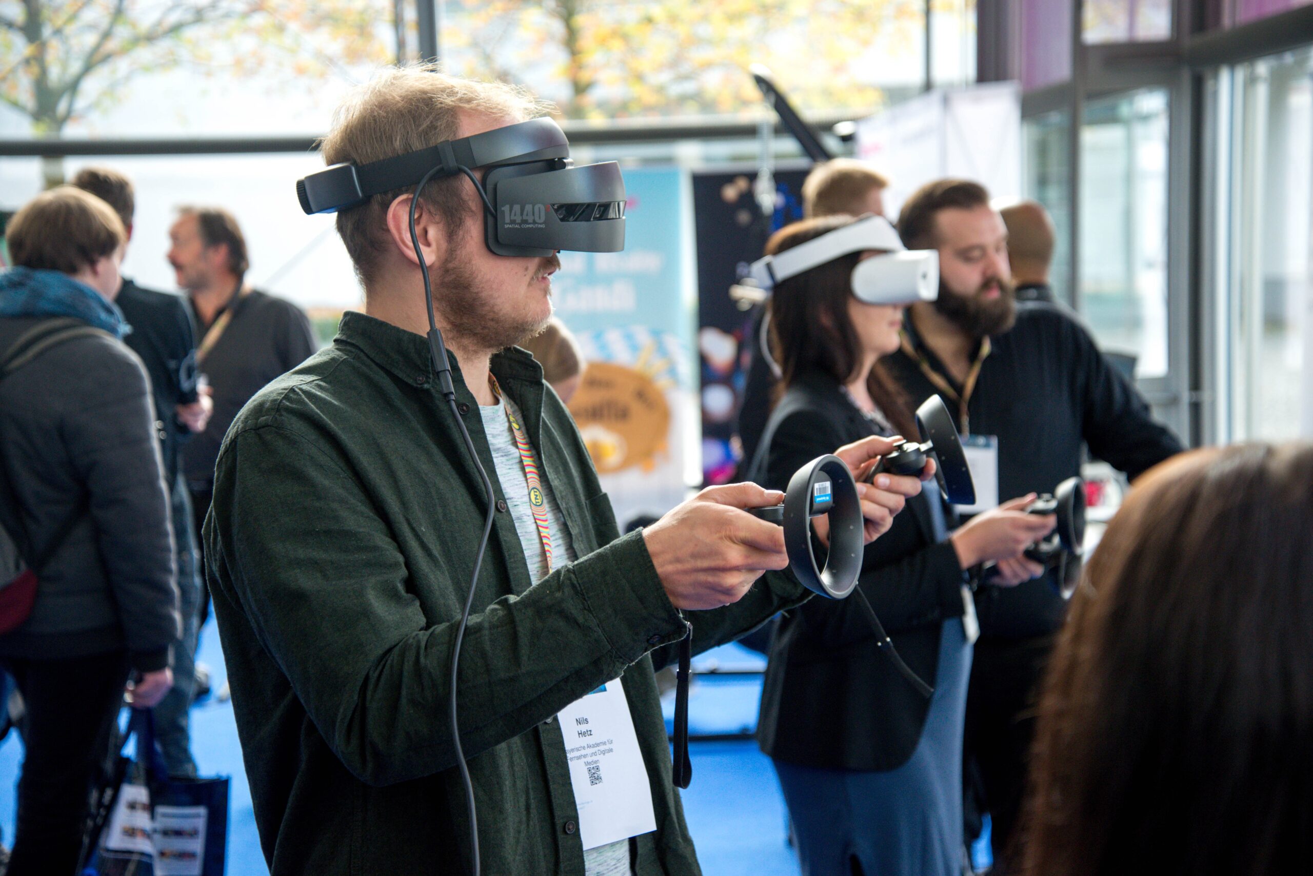Um homem usando um headset de realidade virtual e controladores de mão, com outras pessoas ao seu redor também usando headsets VR.