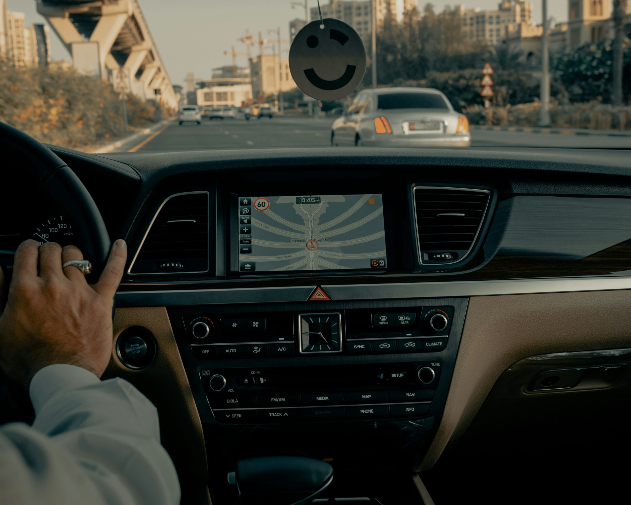 Interior de carro mostrando painel, GPS com mapa de rota, e mão no volante dirigindo em uma estrada urbana sob um viaduto.