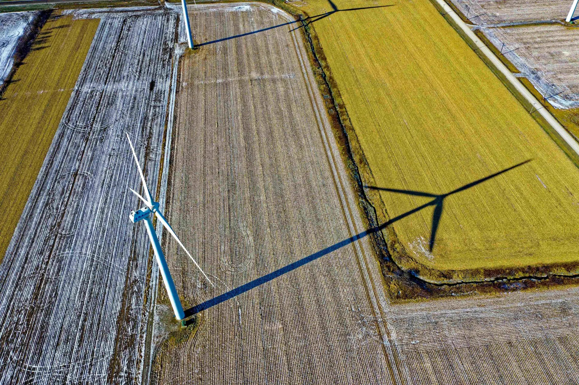 Vista aérea de turbinas eólicas em campo agrícola com sombras longas projetadas no solo. Foco em energia limpa e sustentável.