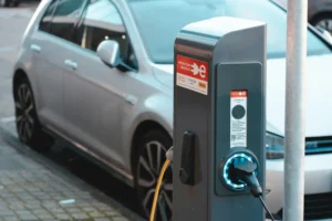 Totem de carregamento de veículos elétricos com luz azul conectado a um carro prata estacionado na rua em Amsterdã.