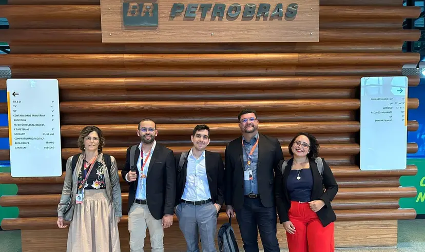 Cinco profissionais sorridentes posam em frente a um painel de madeira com o logotipo da Petrobras em um saguão moderno