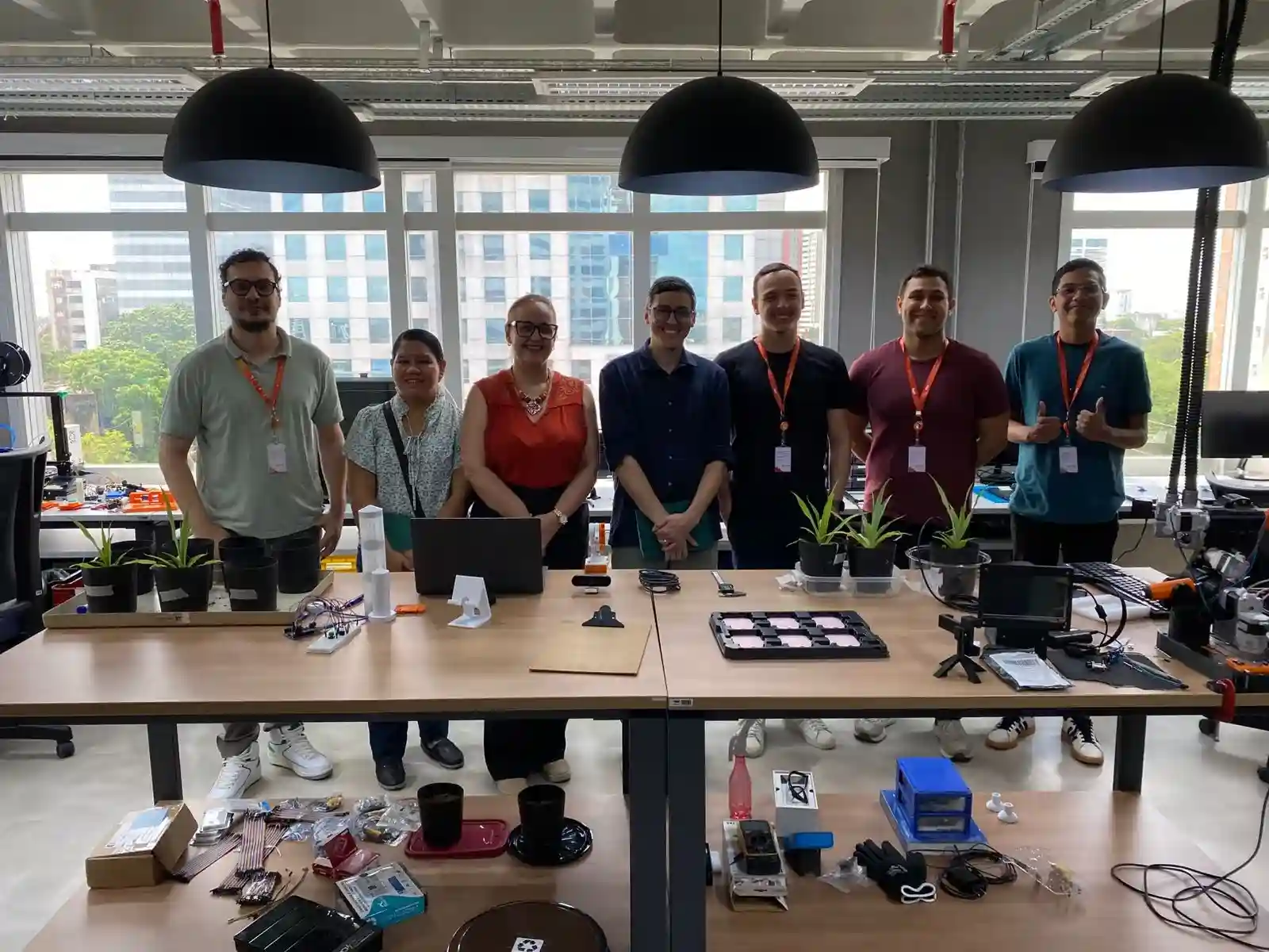 Sete profissionais posam atrás de bancadas com mudas de plantas e componentes eletrônicos num laboratório moderno