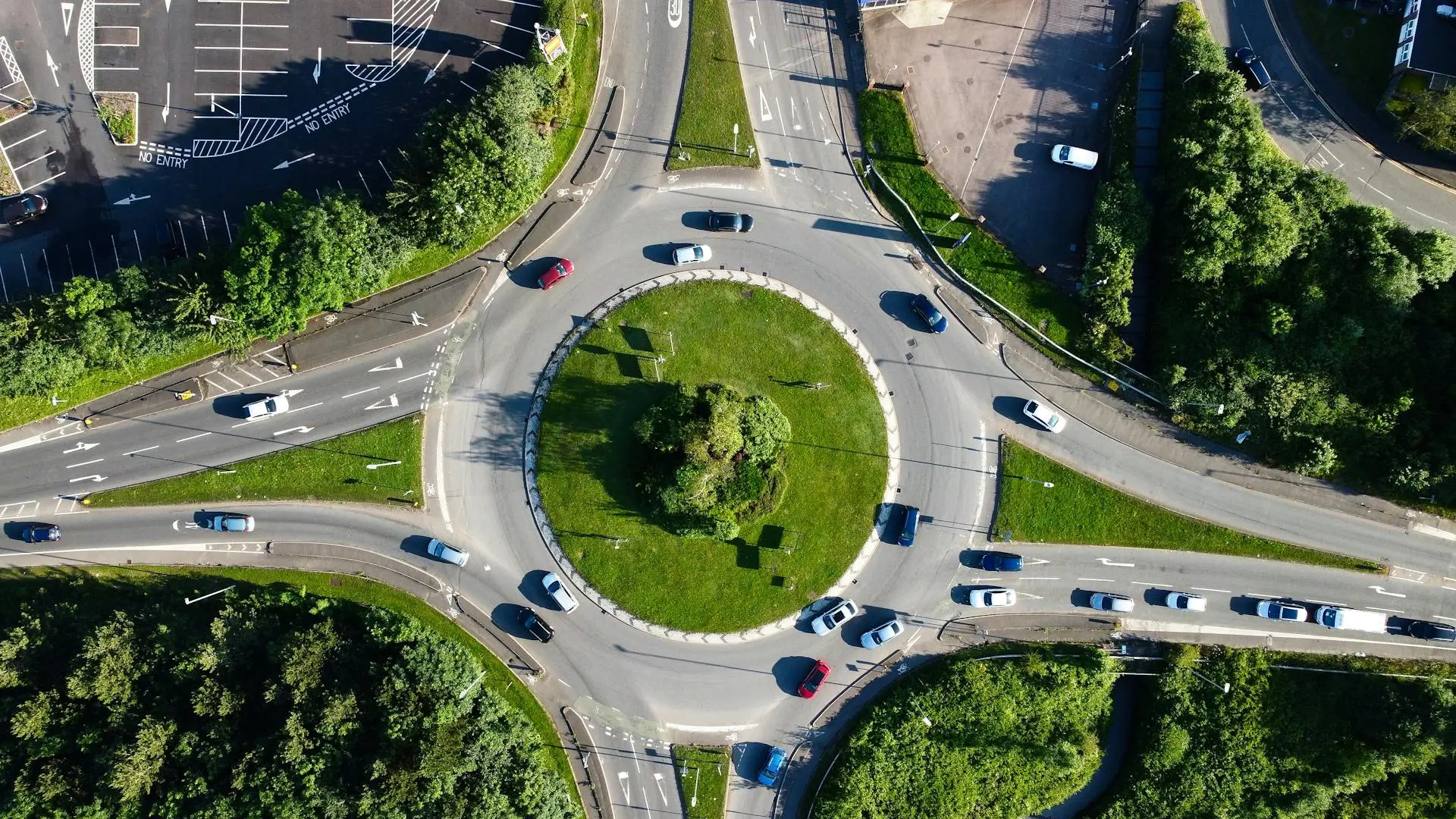 Vista aérea de rotatória gramada com carros circulando entre vias arborizadas, representando o fluxo da mobilidade sustentável.