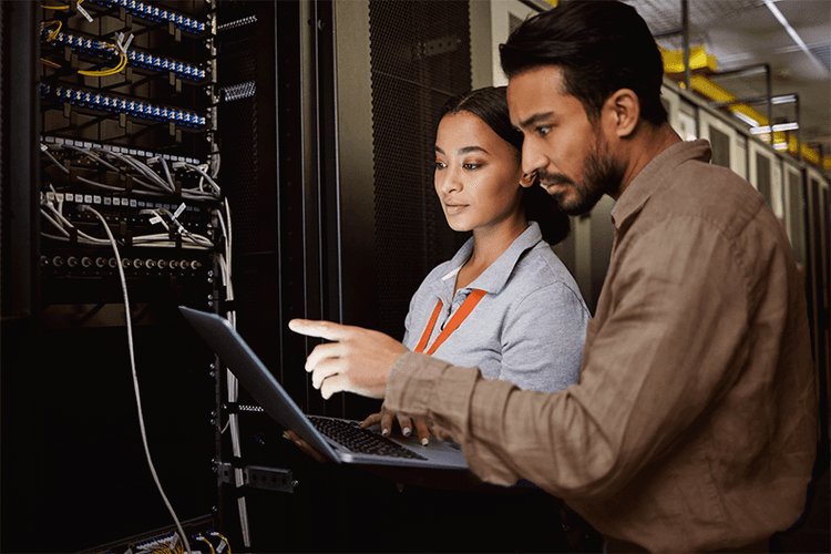 IMAGEM OIL AND GAS pequena@0.1x Um homem e uma mulher olhando para o notebook em uma sala de servidor