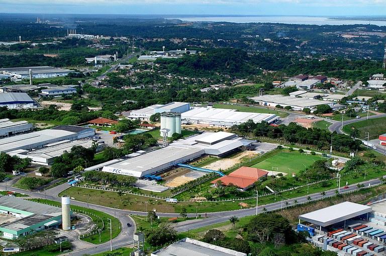 Inovação industrial no Polo de Manaus Vista aérea de galpões industriais brancos cercados por vegetação abundante no Polo de Manaus sob céu com nuvens