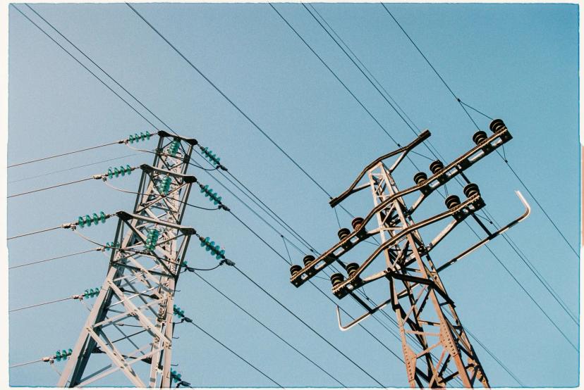 Redução de riscos no setor elétrico com tecnologia e IA aplicada Duas torres de transmissão de energia de metal sob céu azul claro, destacando cabos de alta tensão e isoladores de cerâmica.