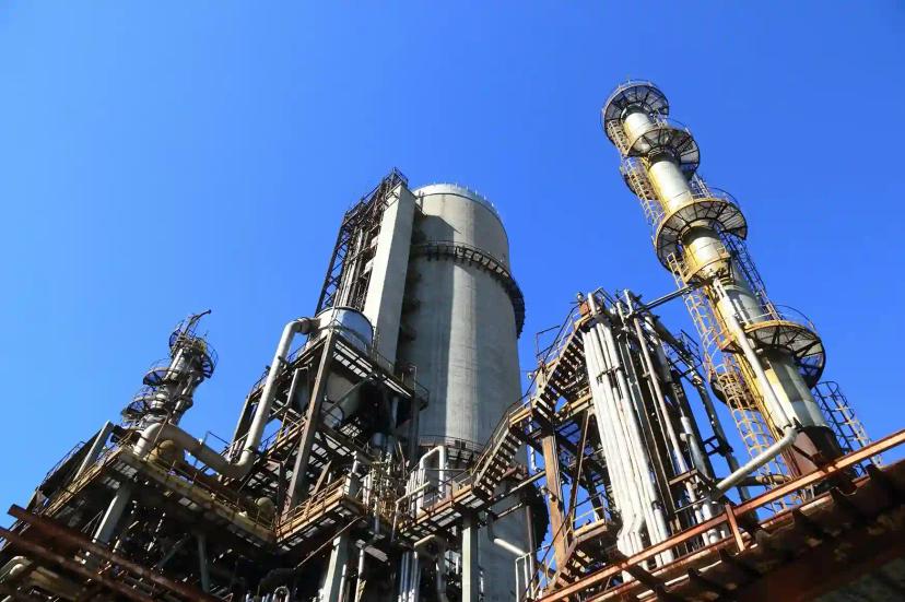 Integração-em-Óleo-e-Gás-Sistemas-Conectados-para-Decisões-Ágeis Torres de destilação e tubulações industriais sob céu azul, representando a infraestrutura de integração em Óleo e Gás.