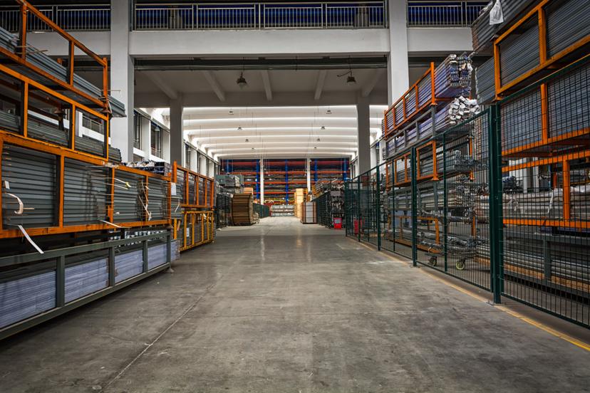 Gestão da inovação na indústria para manufatura inteligente Corredor de galpão industrial com estantes metálicas e materiais armazenados, representando a gestão da inovação na indústria.