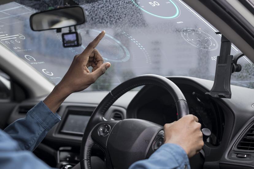 mobilidade-inteligente-e-veiculos-conectados Motorista conduz um veículo e interage com uma interface digital exibida no para-brisa com informações de navegação e velocidade.